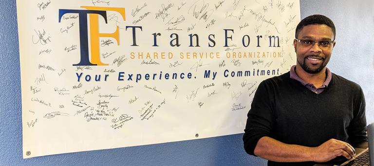 Amos Hanson standing by a banner signed by staff