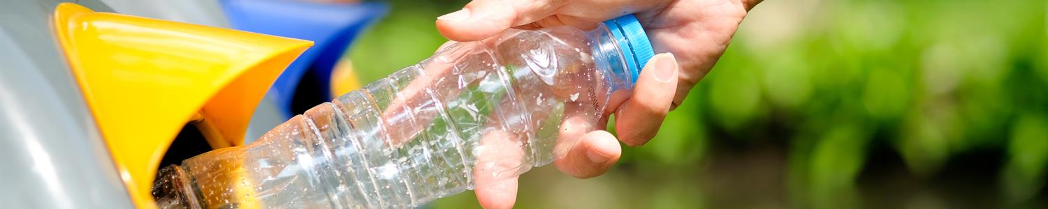 hand placing an empty plastic water bottle into recycling container