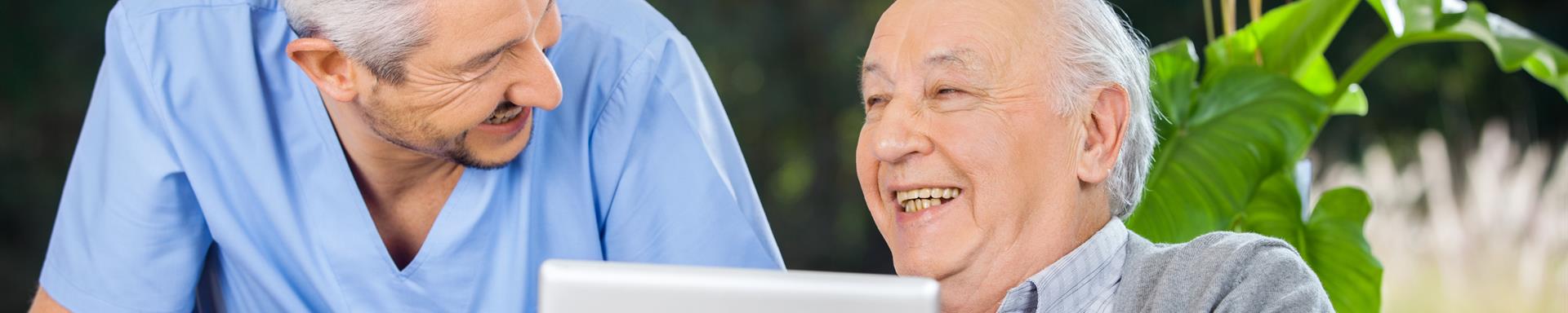 Male caretaker and senior man laughing while using tablet computer at nursing home porch
