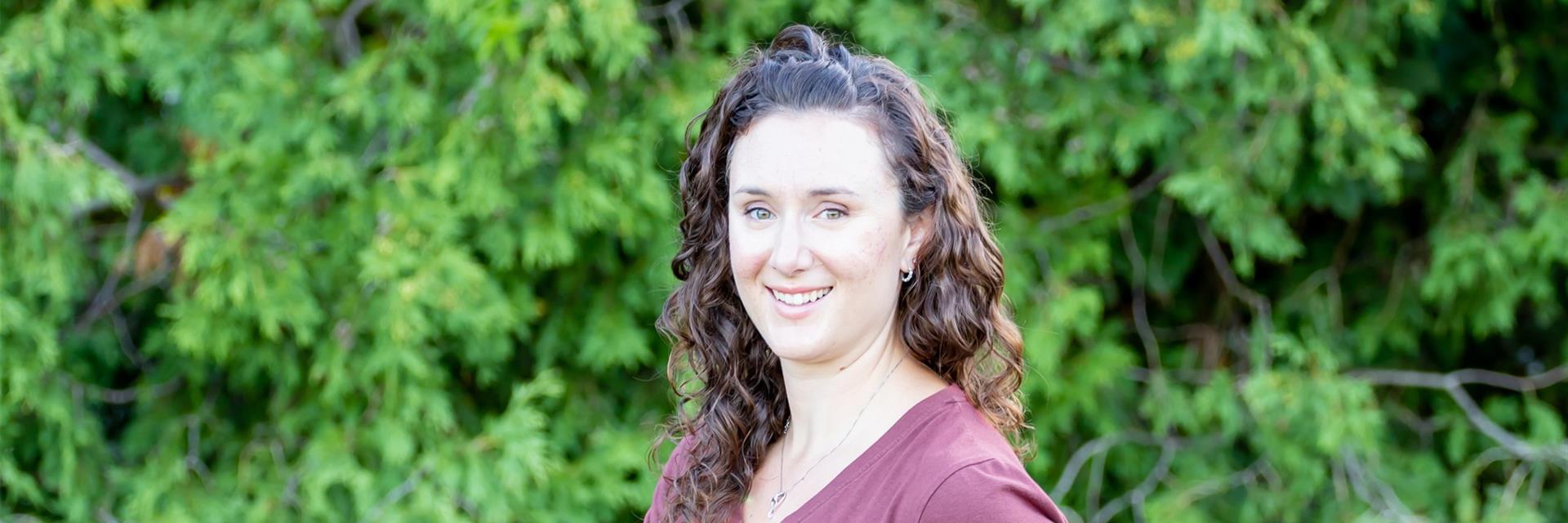 Person smiling in front of a row of trees.