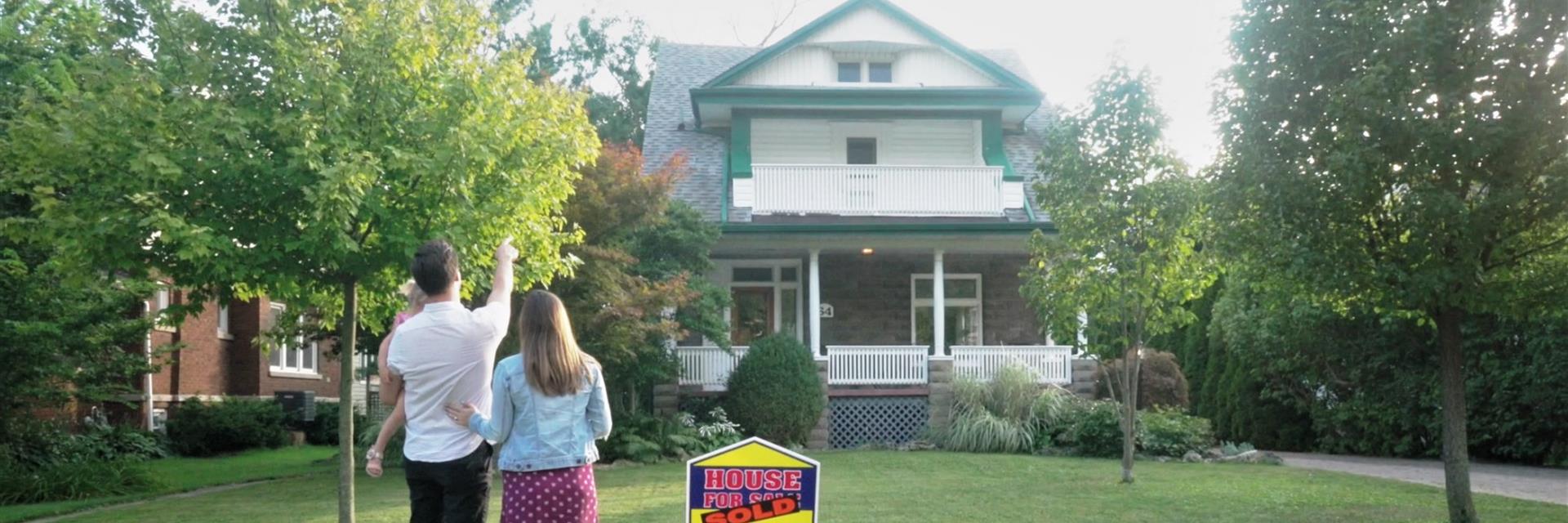 Family looking at their house with a sold sign in the lawn.