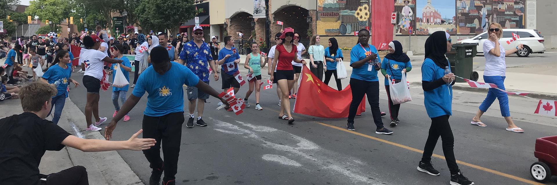 Group of people in a parade wearing blue shirts and waving Canadian flags.