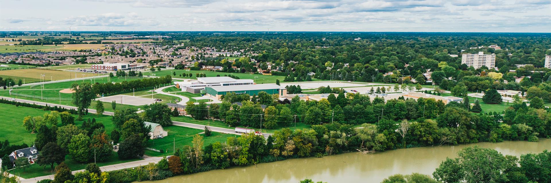 A drone shot of a river surrounded by tall trees throughout residential and commercial streets.