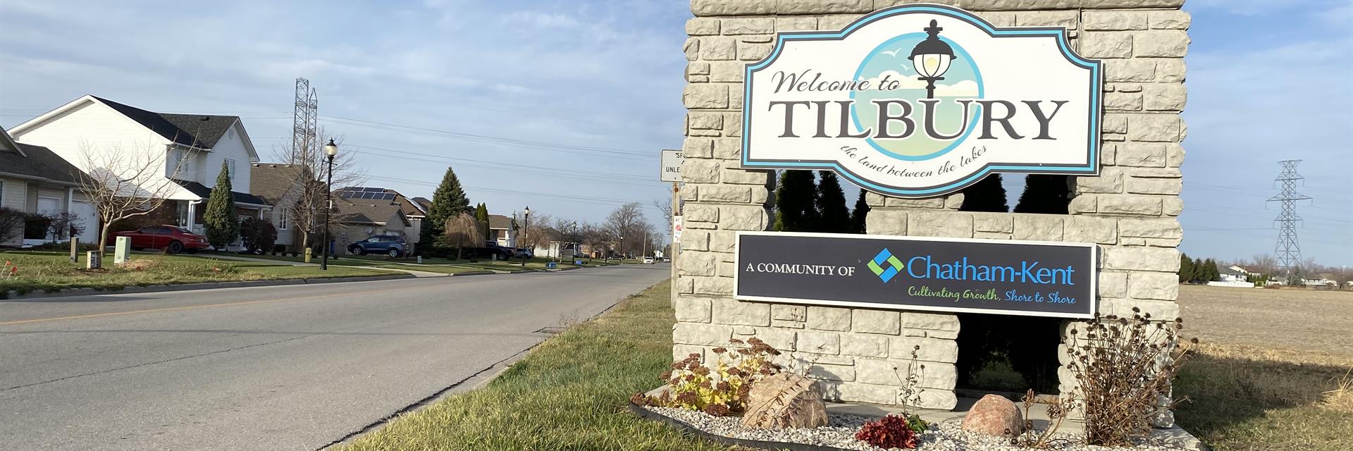 A stone welcome to Tilbury sign on a residential road lined with houses.