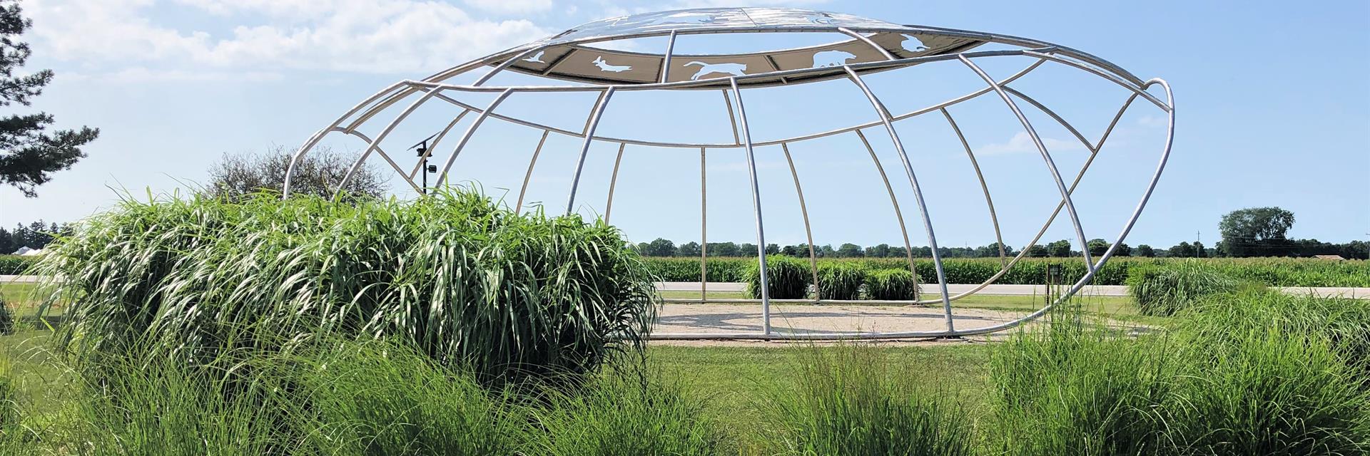 Place of Many Grasses metal sculpture surrounded by tall grasses.