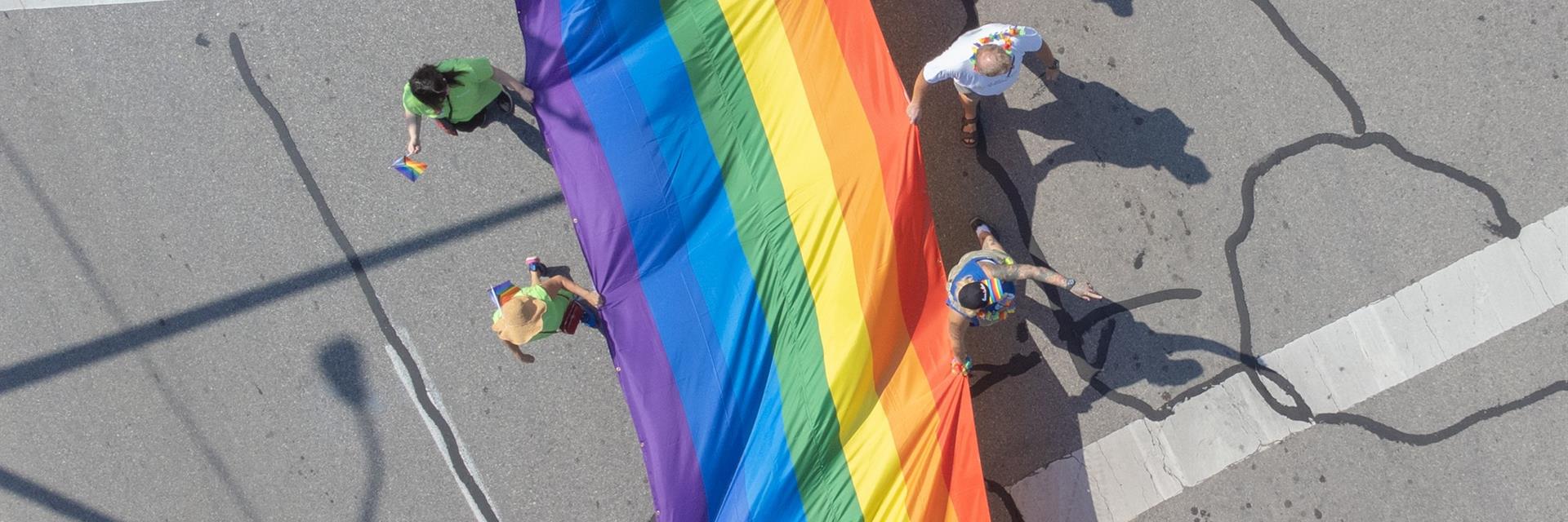 Group of people carrying a large pride flag down the street.