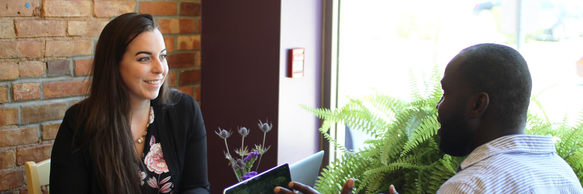 Two people meeting at a cafe with laptops on the table and a notebook.