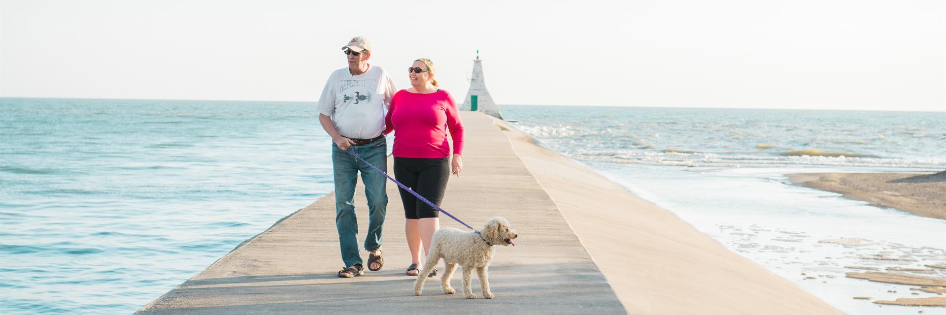 A senior couple walking down the Erieau pier with their dog.