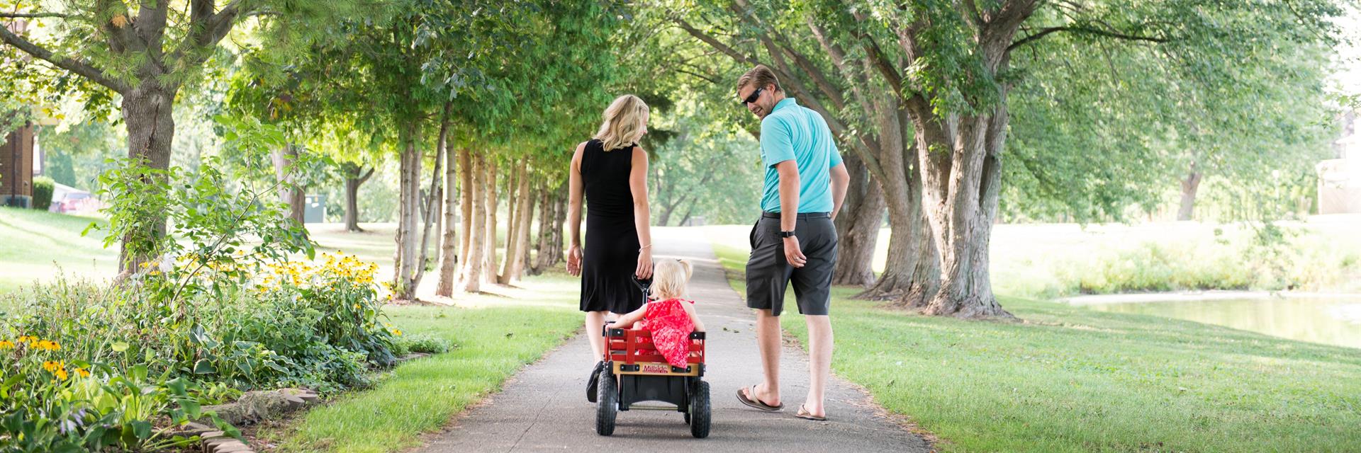 Family walking on a path with a young child being pulled in a wagon.