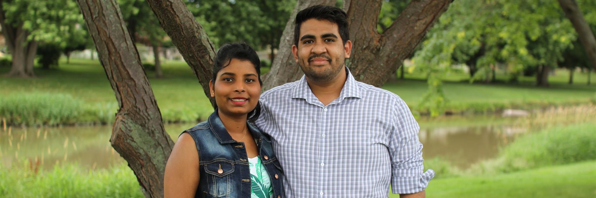 A couple standing in front of greenery.