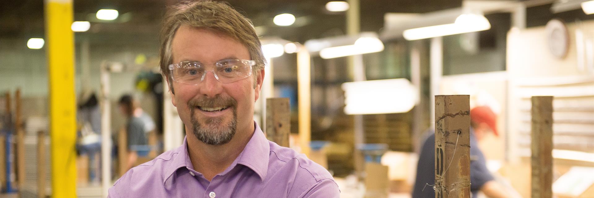 Employer in safety glasses standing on a manufacturing floor.