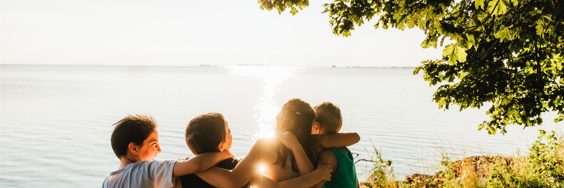 family on picnic table under tree by water on sunny day 