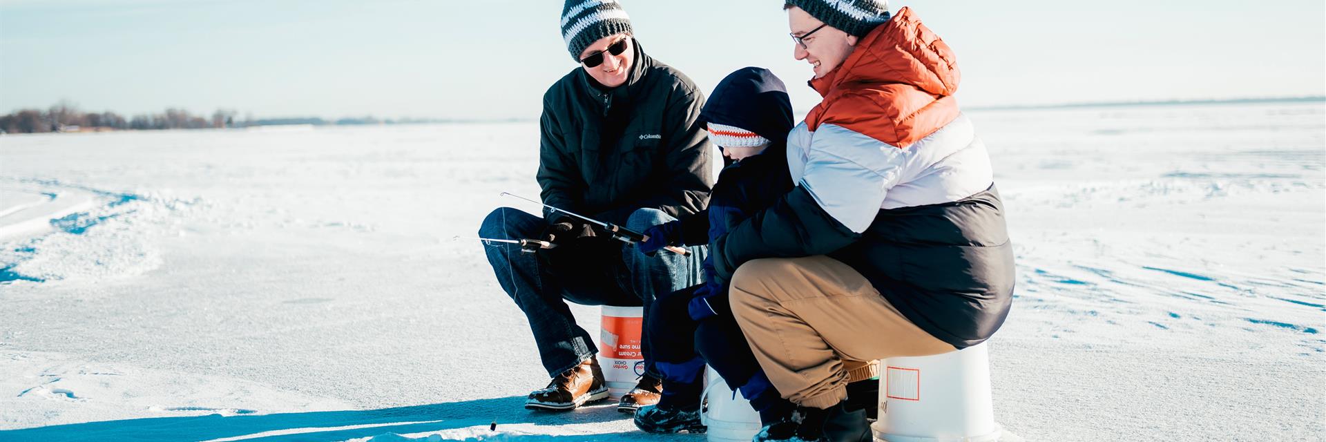male couple and son ice fishing on sunny winter day 